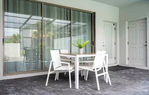 Une pièce dotée d’une porte-fenêtre coulissante, d’une table blanche avec des chaises, d’une plante en pot et d’une porte blanche.