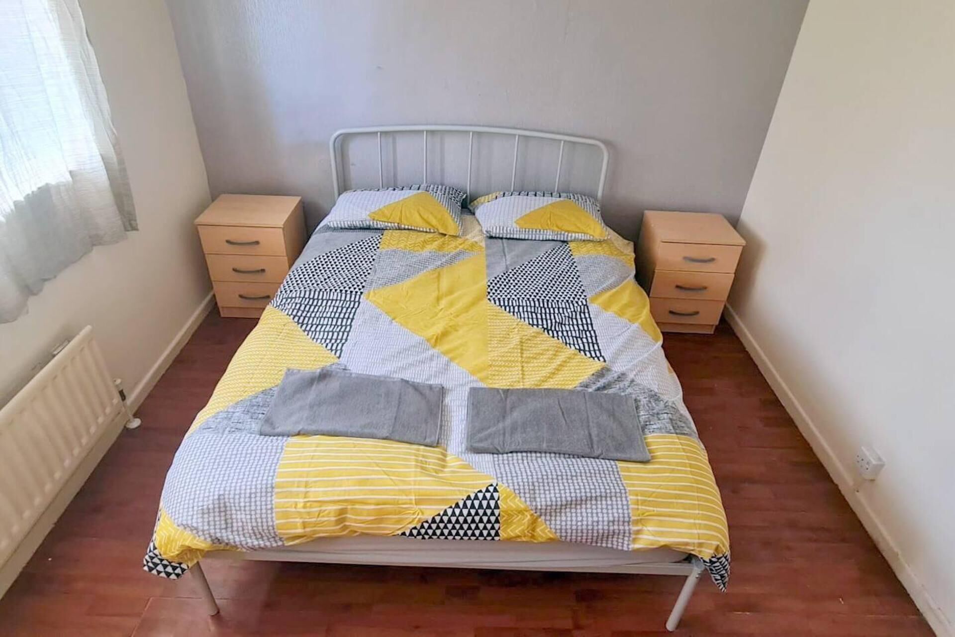 Een bed met een geometrisch beddegoed, twee nachtkastjes en een radiator.