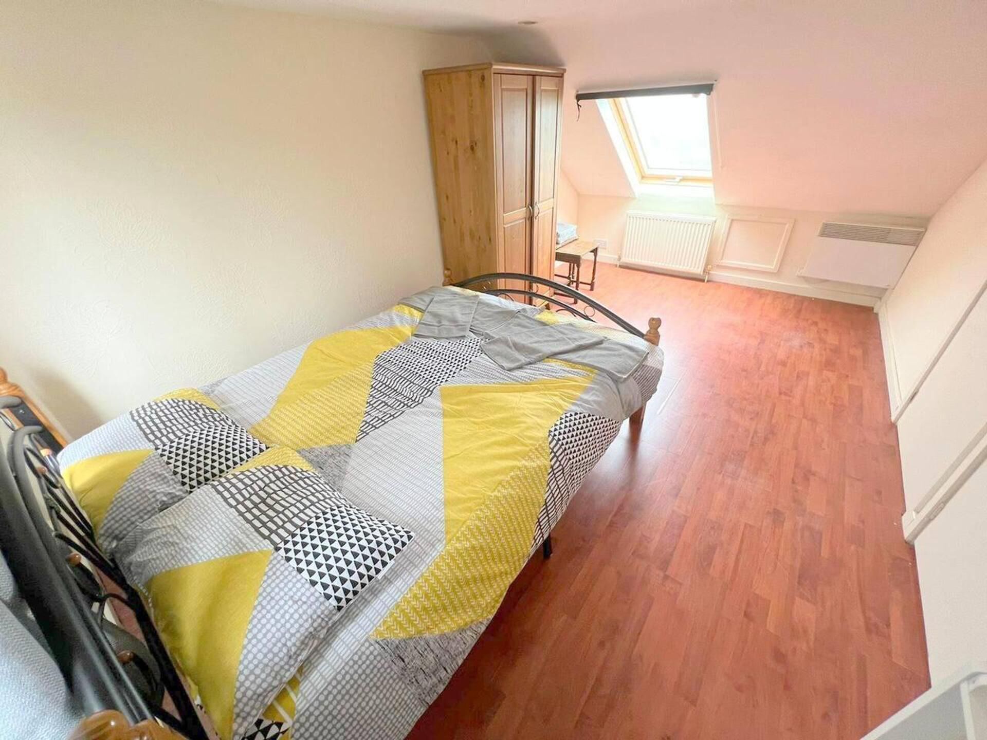 A small, single-bed room with a wooden floor, a window with a view, and a radiator.