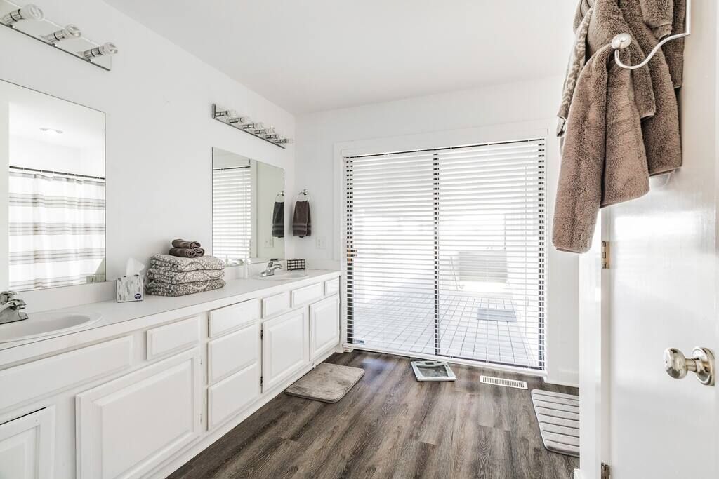 Une salle de bain moderne avec des meubles blancs, un grand miroir et un plancher en bois.