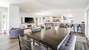 Een moderne woonkamer met een grote, donkerhouten eettafel, grijze banken en een flatscreen televisie.
