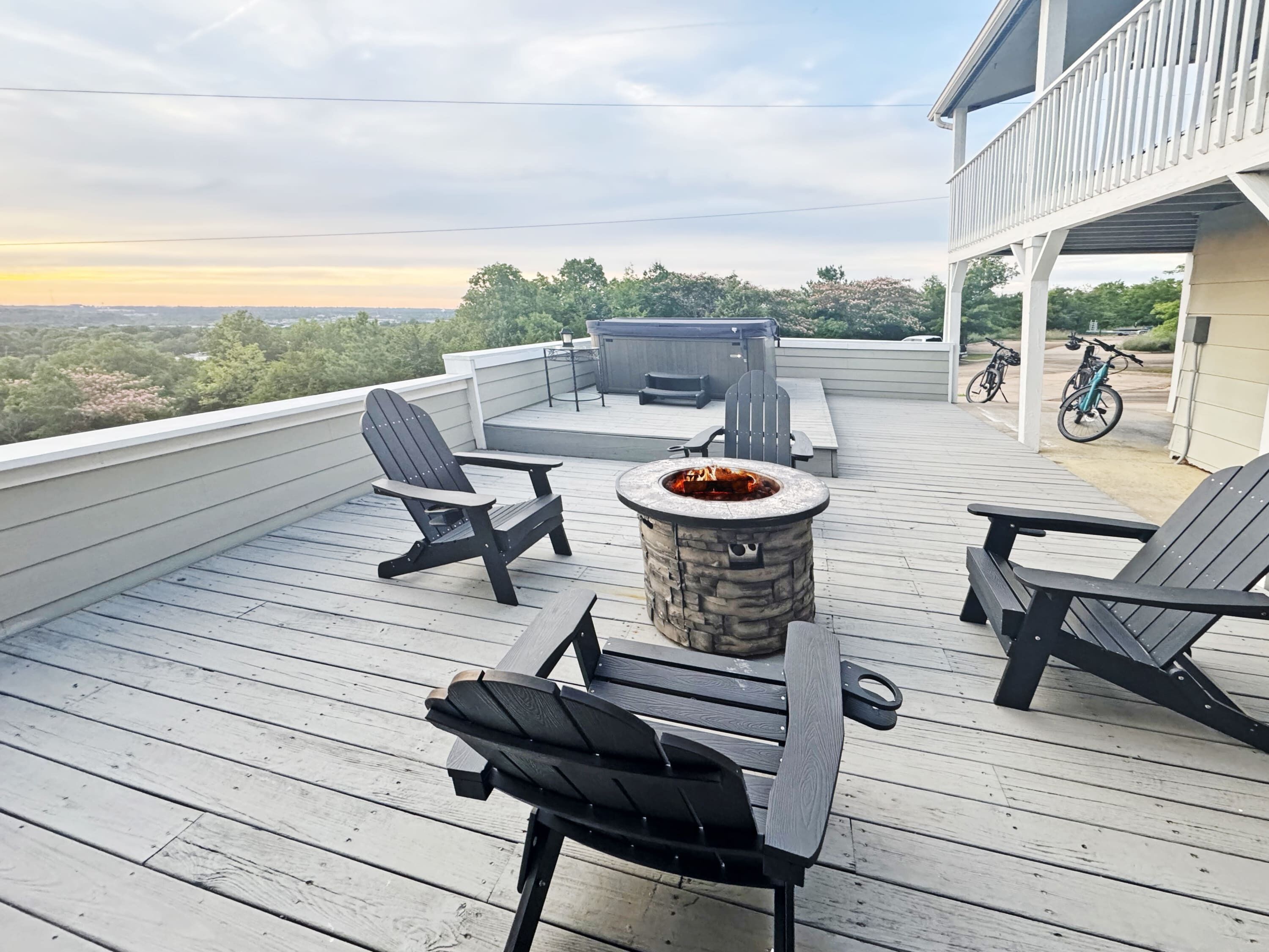 A wooden deck with Adirondack chairs and a stone fire pit.