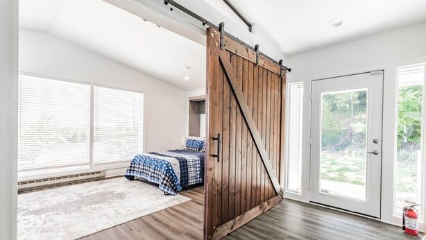Een slaapkamer met een grote schuifdeur in boerderijstijl, een bed met geruit beddengoed en uitzicht op de omgeving via een glazen deur.