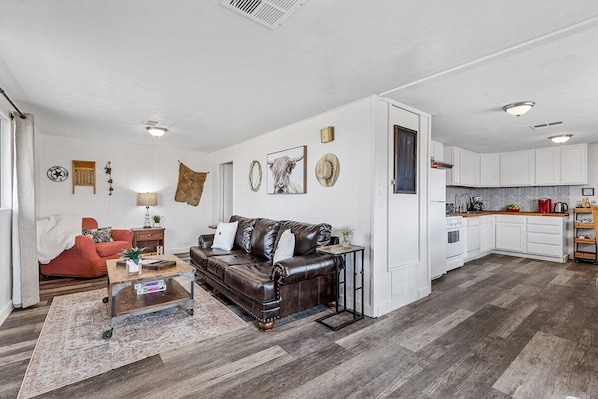 A spacious living area with a leather sofa, a coffee table, and a kitchen in the background.
