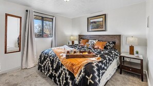 Une chambre à coucher avec un lit, deux tables de chevet, une fenêtre, un tableau et un miroir.