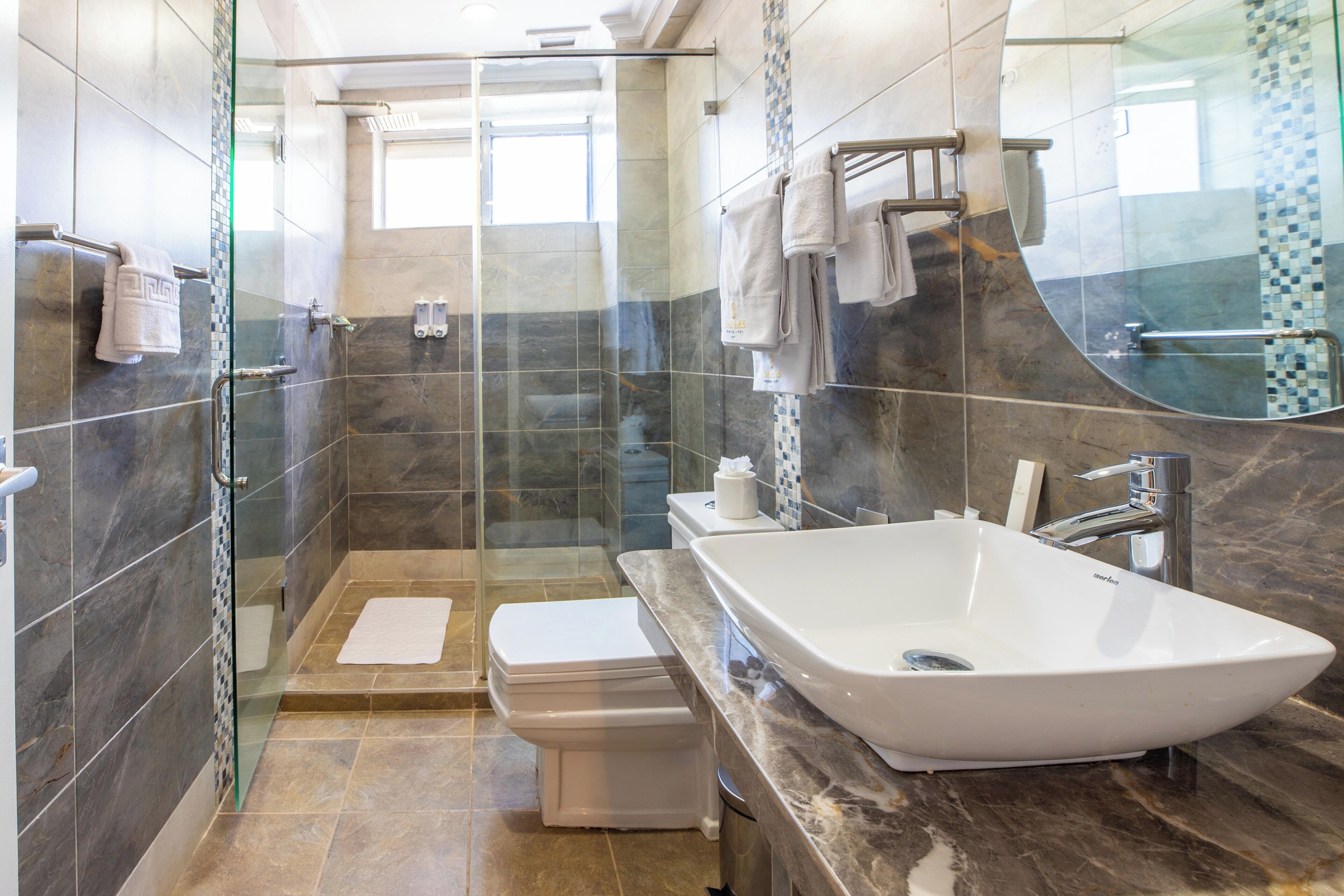 A modern bathroom with a glass-enclosed shower, a large freestanding bathtub, and a marble-tiled vanity.