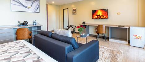 A modern hotel room with a large bed, a sofa, a desk, and a small kitchenette.