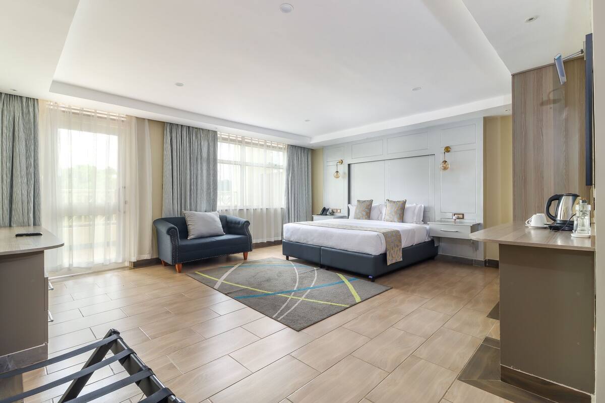 A modern hotel room with a bed, a sofa, a desk, and a large window with curtains.