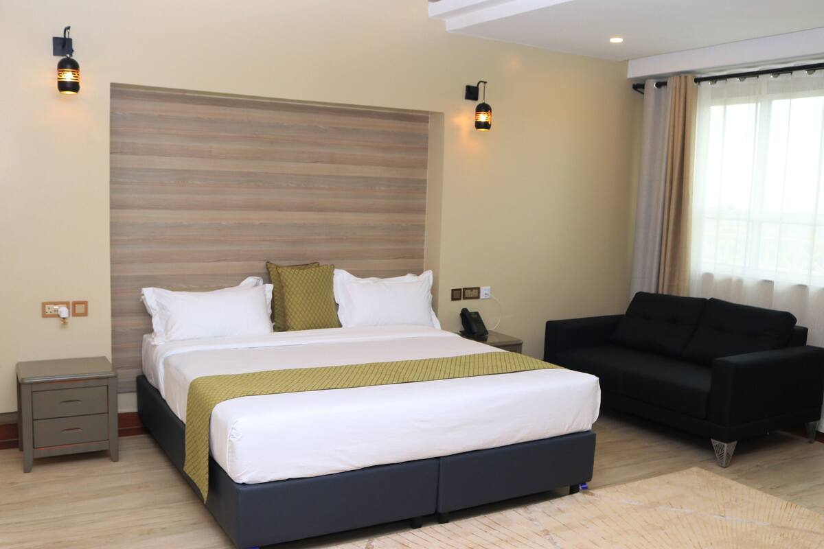 A modern hotel room with a large bed, a sofa, and a wooden headboard.