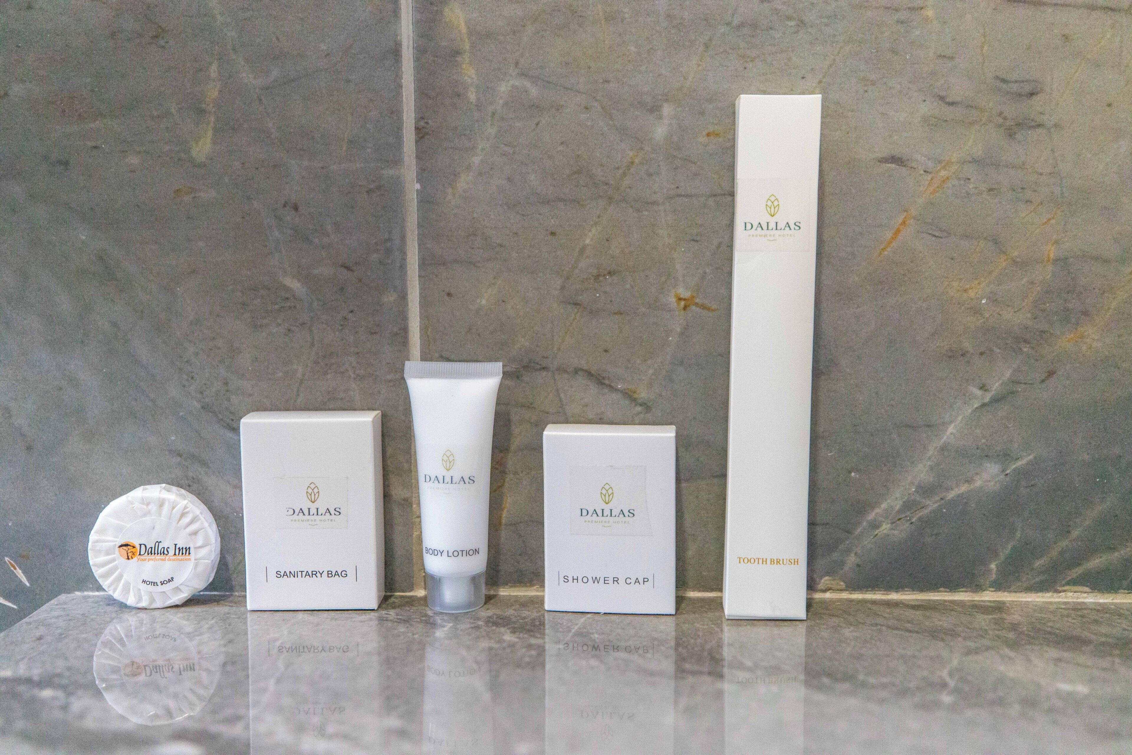 Un conjunto de artículos de tocador que incluye jabón de hotel, loción corporal, gorro de ducha y un cepillo de dientes, todos con el logotipo del Dallas Premiere Hotel.