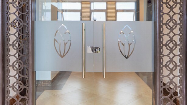 Entrada moderna de hotel con puerta de vidrio que presenta diseños geométricos recortados y un picaporte metálico.