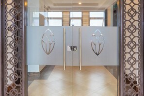 Entrada moderna de hotel con puerta de vidrio que presenta diseños geométricos recortados y un picaporte metálico.