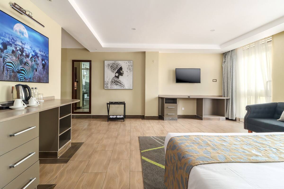 A hotel room with a bed, a desk, a television, and artwork on the walls.