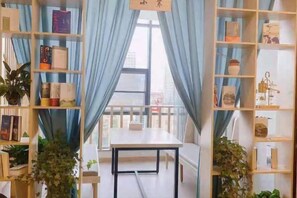 Una habitación con una mesa blanca, cortinas azules y estanterías con libros y objetos decorativos.