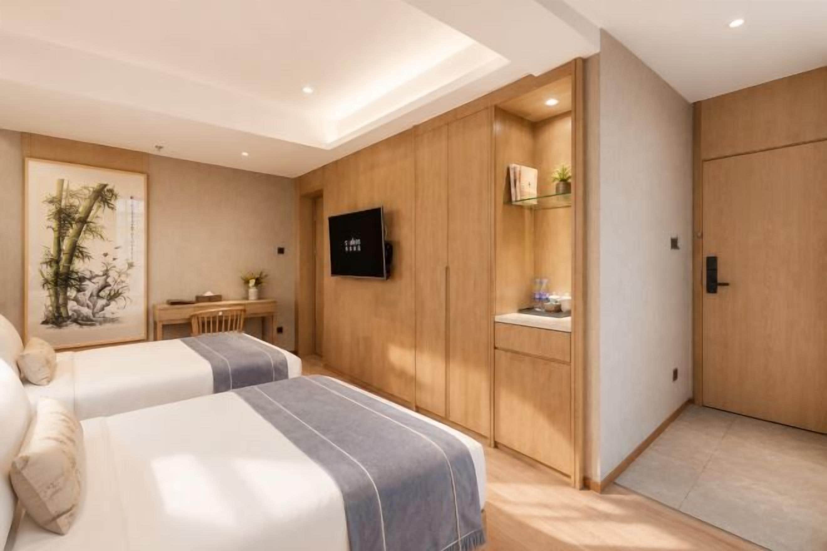 A hotel room with two beds, a desk, a TV, and a wardrobe.
