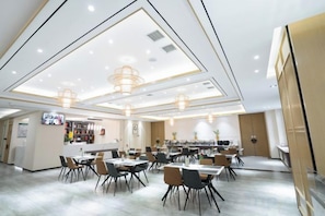 A modern dining area with multiple tables and chairs, recessed ceiling lights, and a bar area in the background.
