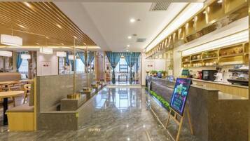 A modern hotel lobby with a marble floor, a reception desk, and a seating area with tables and chairs.