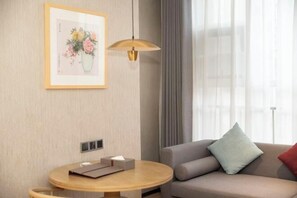 A modern hotel room with a sofa, a round wooden table, a framed artwork, and a pendant light. - Xijian Hotel (Baoji)
