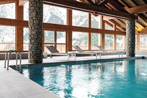 Ein Innenpool mit steinernen Säulen, Holzbalken und großen Fenstern.