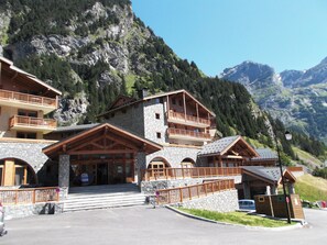 A multi-story mountain lodge with stone and wood construction, balconies, and a parking area. - Lagrange Vacances Les Hauts de la Vanoise (Pralognan-la-Vanoise)