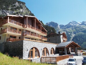 Un immeuble à plusieurs étages, doté de balcons, de murs en pierre et surplombant un paysage montagneux.