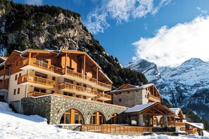 Un chalet à plusieurs étages, doté de balcons, d’une fondation en pierre et surplombant un paysage montagneux.