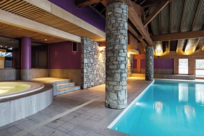 Une piscine intérieure avec des piliers en pierre, un jacuzzi et un plafond en bois.