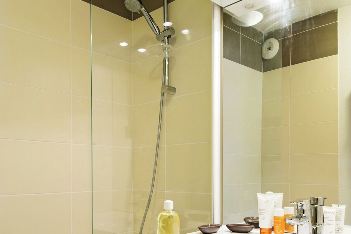 A modern bathroom with a glass-enclosed shower, a white vanity with a mirror, and toiletries on the counter.