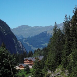 Eine Berghütte mit mehreren Holzhäusern, umgeben von dichtem Wald und Bergen.