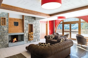 A cozy living room with a stone fireplace, a large sofa, and a view of a snowy landscape through large windows. - Lagrange Vacances Les Hauts de la Vanoise (Pralognan-la-Vanoise)