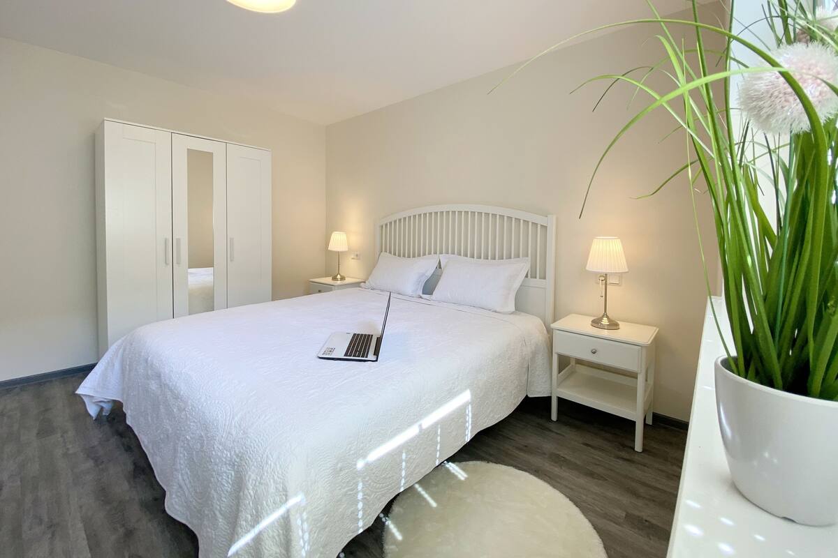 A neatly arranged bedroom with a bed, bedside tables, a wardrobe, and a potted plant.