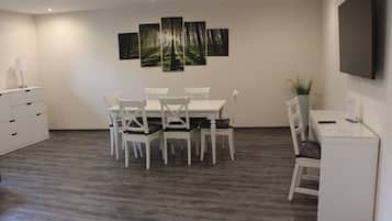 A modern room with a dining table, four chairs, a white desk, and a flat-screen TV mounted on the wall.