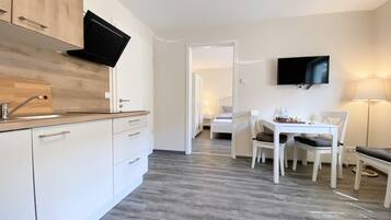 A modern kitchen with a built-in TV, a dining area with a chessboard, and a bedroom visible through an open door.