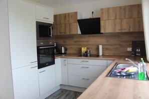 A modern kitchen with white and wooden cabinets, stainless steel appliances, a microwave, and a sink with a dish rack. - Regiohotel Pfälzer Hof Wernigerode (Wernigerode)
