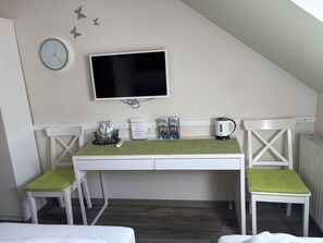 A hotel room with a TV mounted on the wall, a desk with chairs, a kettle, and a clock. - Regiohotel Pfälzer Hof Wernigerode (Wernigerode)