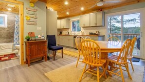 Une cuisine chaleureuse avec des meubles en bois, une table à manger entourée de chaises et une vue sur l’extérieur grâce à de grandes fenêtres.