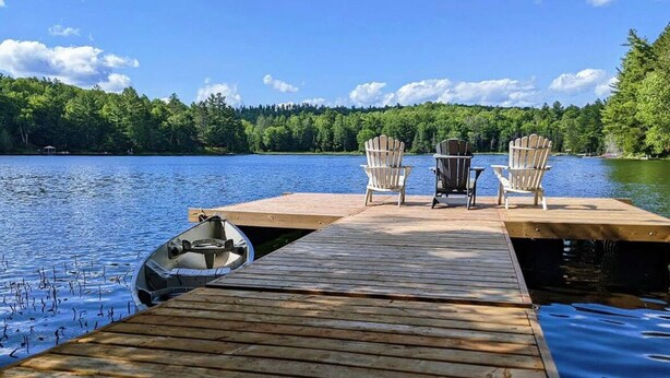 Une jetée en bois s’avançant dans un lac, avec deux chaises Adirondack et un bateau.