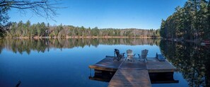 Relax on the lakeside dock with Adirondack chairs and a table, surrounded by a dense forest.