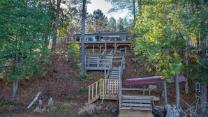Une cabane dotée d’une terrasse en bois et d’un quai s’avançant dans l’eau, le tout entouré d’arbres.