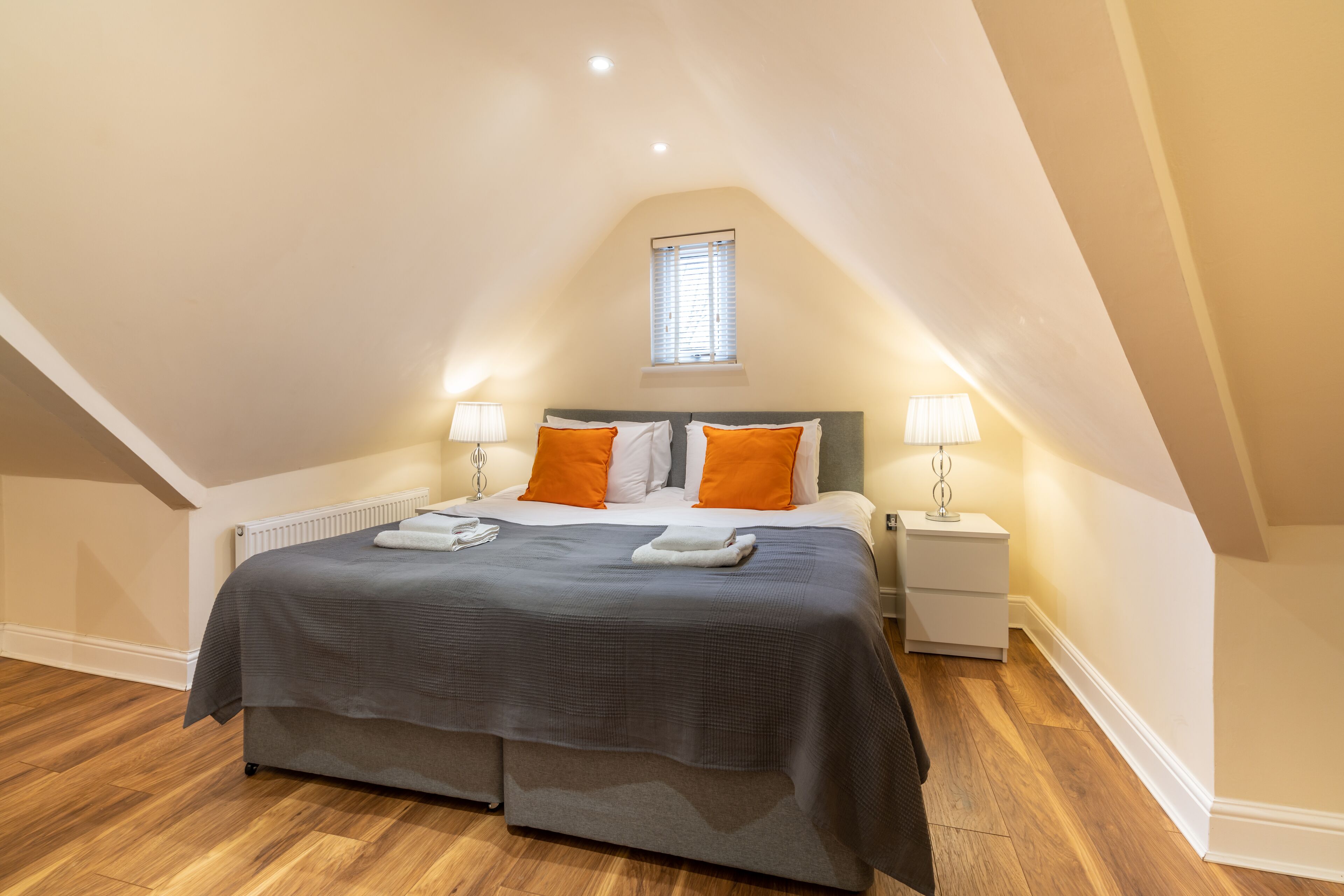 A bedroom with a large bed, two bedside tables, a window, and a radiator.