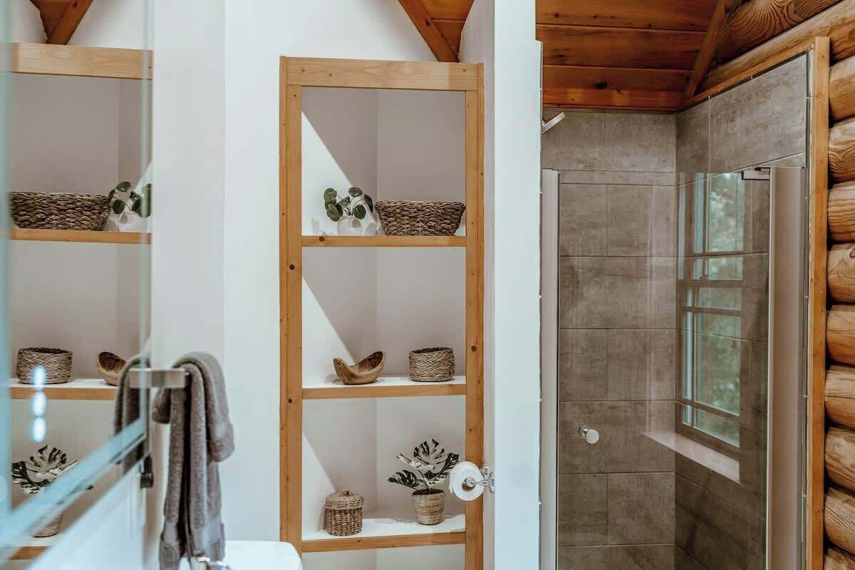 Un baño con estantes de madera, toallero y zona de ducha con ventana.