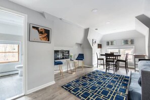 Ein modernes Wohnzimmer mit einem blauen Teppich mit Muster, einem grauen Sofa und einem Essbereich mit Tisch und Stühlen.
