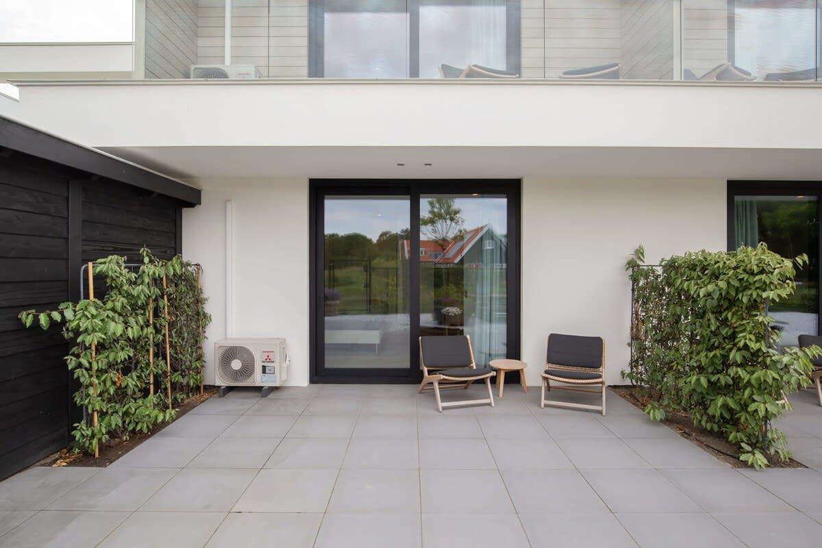 Un patio moderno al aire libre con dos sillones, una puerta de vidrio y una pared negra en un lateral.