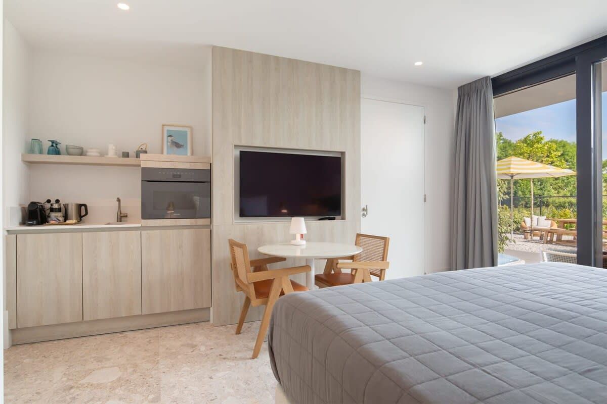 Una habitación de hotel moderna con una cama grande, una kitchenette, un comedor y un televisor.