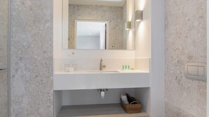 A modern bathroom with a marble backsplash, a large mirror, a white sink, and a shelf with toiletries. - Studio near beach in Domburg | Summum Suites 2 (Domburg)