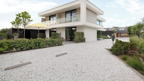 A modern two-story house with a covered patio, gravel driveway, and surrounding greenery. - Studio near beach in Domburg | Summum Suites 2 (Domburg)