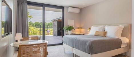 A modern bedroom with a large bed, a bedside table with a lamp, a chair, and a view of the outdoors through a sliding door.