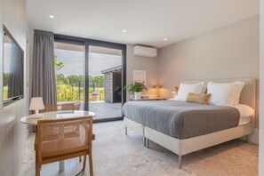 A modern bedroom with a large bed, a small table, and a chair. There is a balcony with a view of greenery. - Studio near beach in Domburg | Summum Suites 2 (Domburg)