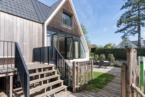 Une maison moderne avec une façade en bois, une terrasse dotée d’un escalier et une cour arrière clôturée.
