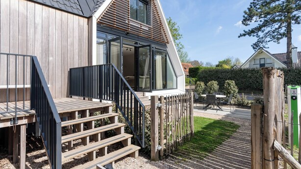 Ein modernes Haus mit Holzfassade, einer Terrasse mit Treppe und einem eingezäunten Garten.